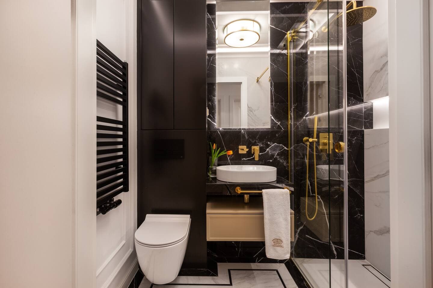 Modern bathroom w/ dark marble accents, glass shower & warm ambient lighting